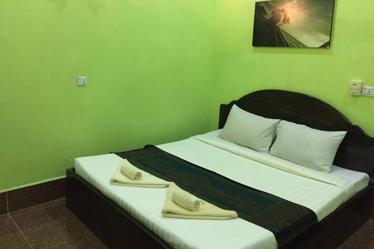 A bed with a white mattress and pillows, a dark headboard, and a green wall.