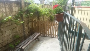 Un banco de madera, una reja de metal y una planta en maceta en un patio con un muro de piedra y una valla de madera.