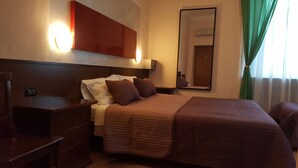Una habitación de hotel con una cama grande, una mesita de noche, un aparador, un espejo y una ventana con cortinas.