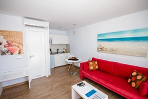 Un salón moderno con un sofá rojo, una mesa de centro blanca y un cuadro con una playa.