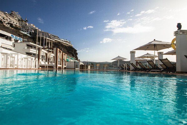 Una piscina al aire libre, sombrillas, sillones reclinables de piscina