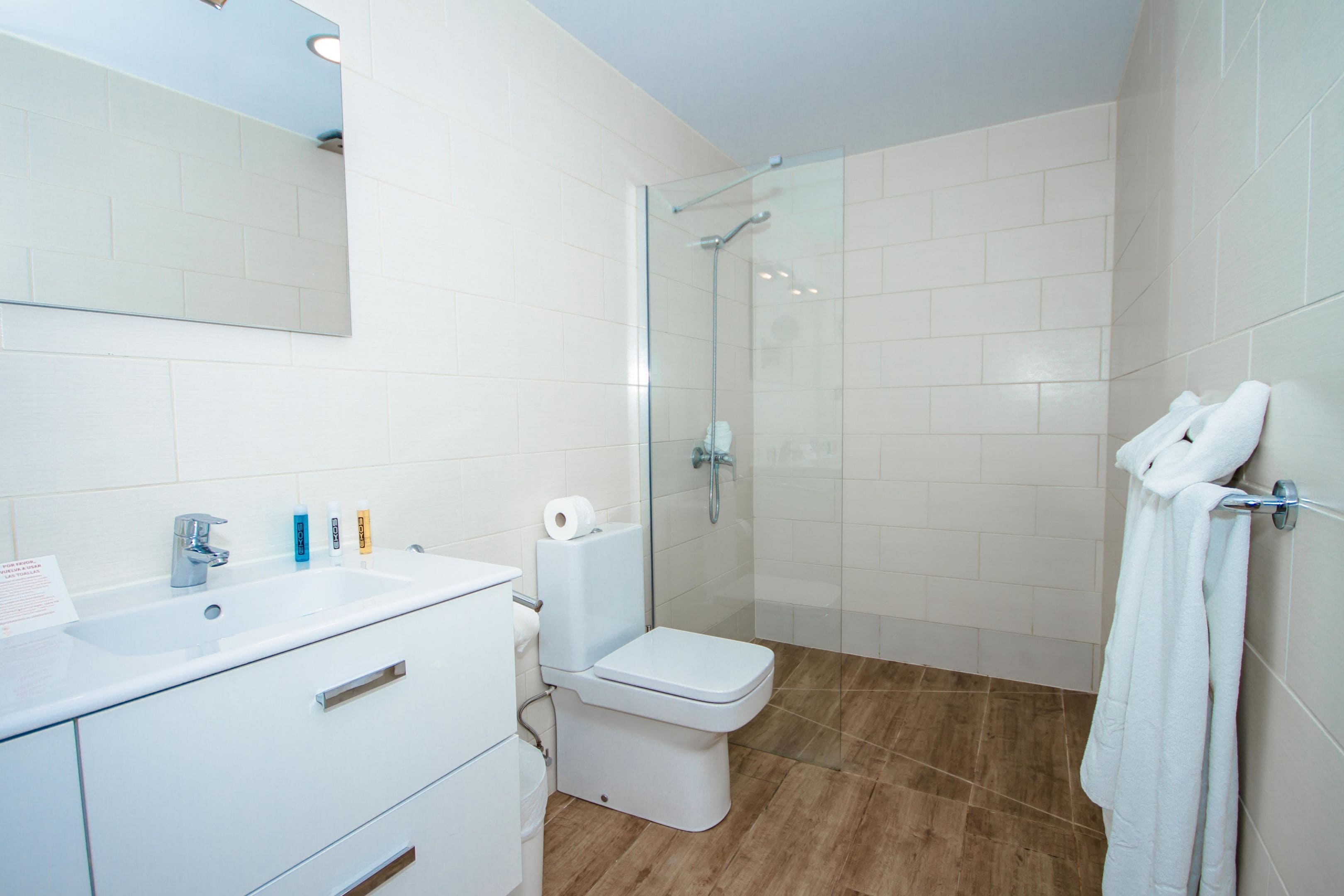 Un baño moderno con lavamanos blanco, inodoro y cabina de ducha con paredes de vidrio.