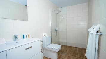 Un baño moderno con lavamanos blanco, inodoro y cabina de ducha con paredes de vidrio.