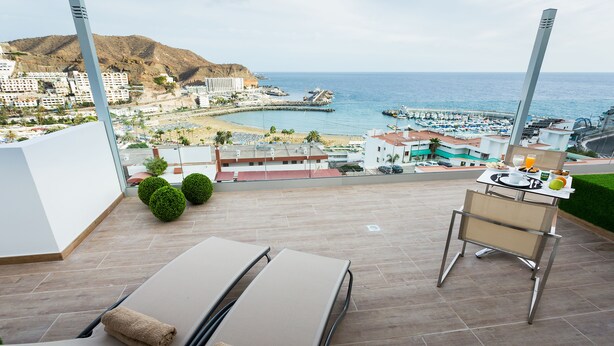 Un balcón con dos tumbonas, una mesa con desayuno y vista a la playa y al océano.