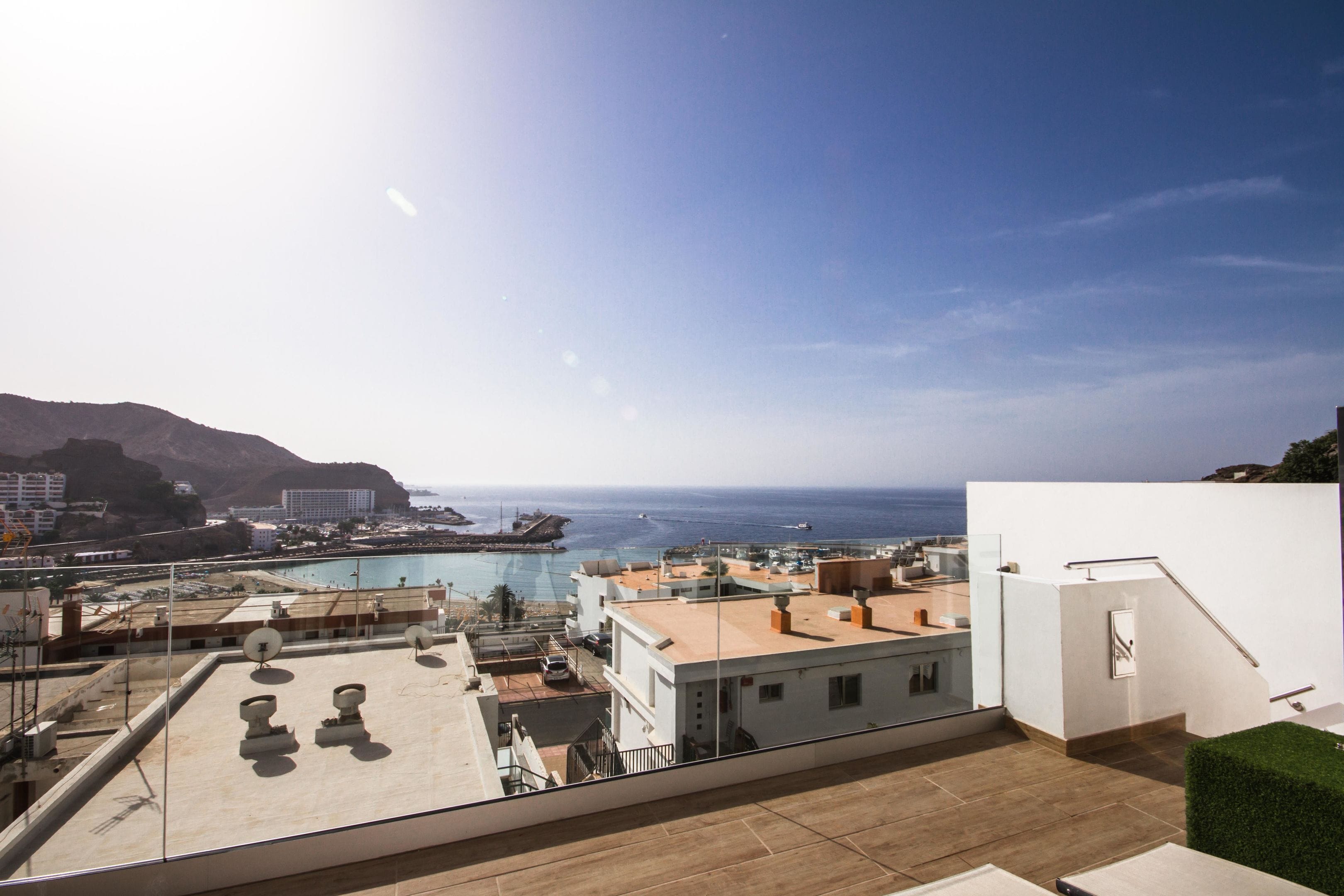 A rooftop terrace with a view of the sea and mountains, featuring a pool, satellite dishes, and a staircase.