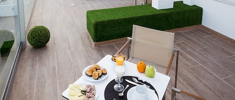 A rooftop dining area with a table set for two, a lounge chair, and a view of the hotel sign.