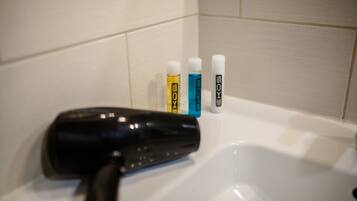 A bathroom with a black hairdryer on a sink, and three bottles of hair care products labeled 'SOKOS' in different colors.