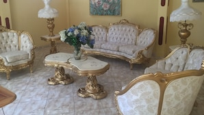 Uma sala de estar luxuosa com móveis ornamentados, piso de mármore e uma pintura na parede.