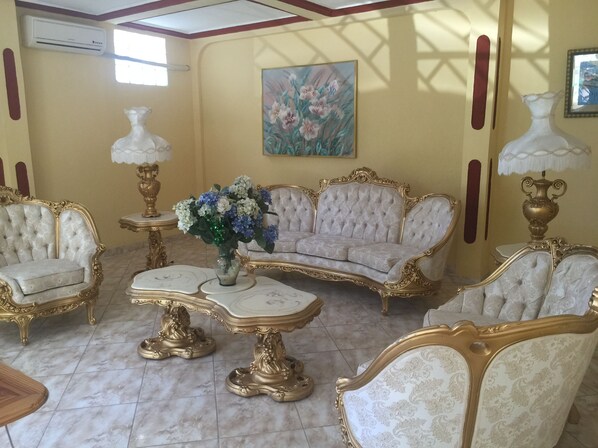 Un salón lujoso con muebles ornamentados, suelo de mármol y un cuadro en la pared.