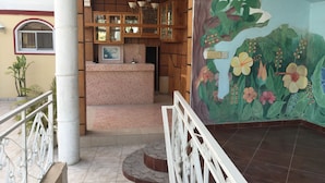 Uma área de recepção com balcão revestido de azulejos, armários de madeira e um mural de flores tropicais.