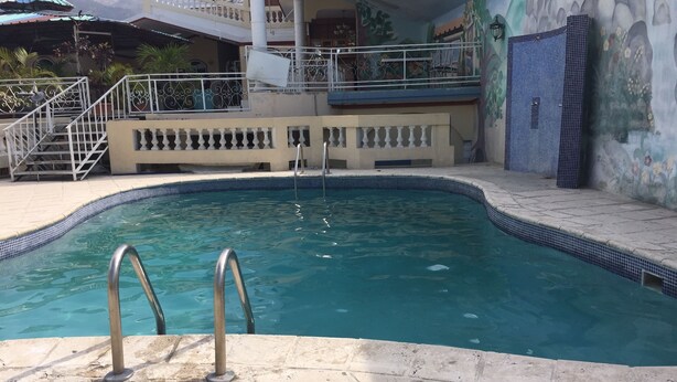 Uma piscina com escadas de metal, um deck revestido de azulejos e um mural na parede.