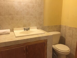 A bathroom with a sink, toilet, and wooden cabinets. - Paradis Hotel (Petionville)