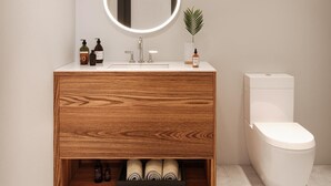 A modern bathroom with a wooden vanity, a mirror with a light, a toilet, and a small plant. - Motel du Lac Beauchamp (Gatineau)