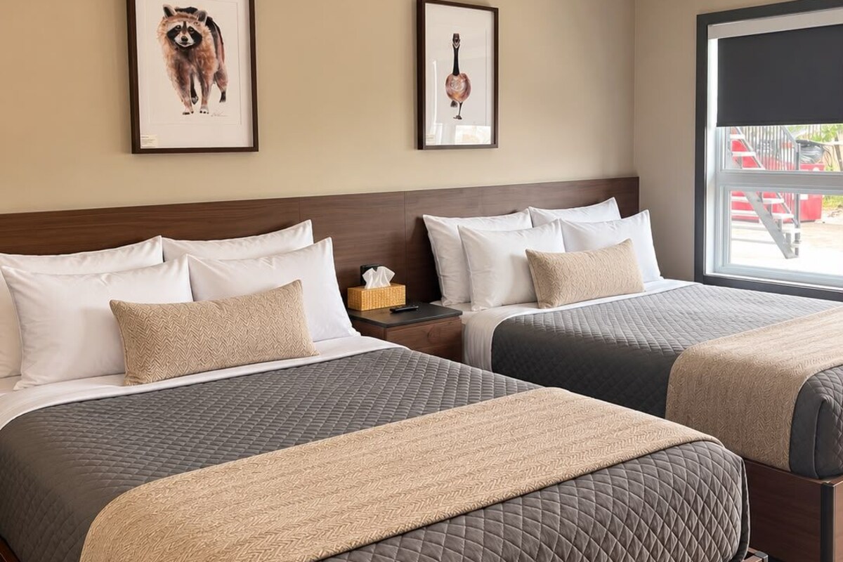 A hotel room with two beds, a wooden headboard, a window with a view, and two framed pictures on the wall.