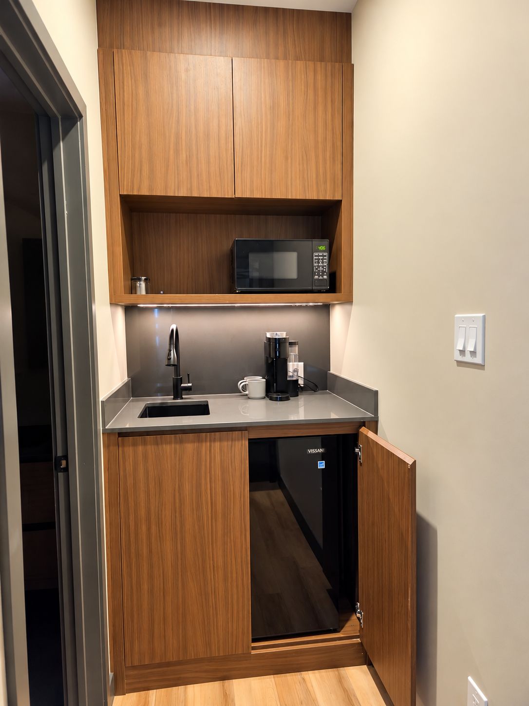 A compact kitchen with wooden cabinets, a microwave, a coffee maker, and a dishwasher.