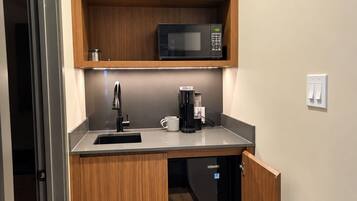 A compact kitchen with wooden cabinets, a microwave, a coffee maker, and a dishwasher.