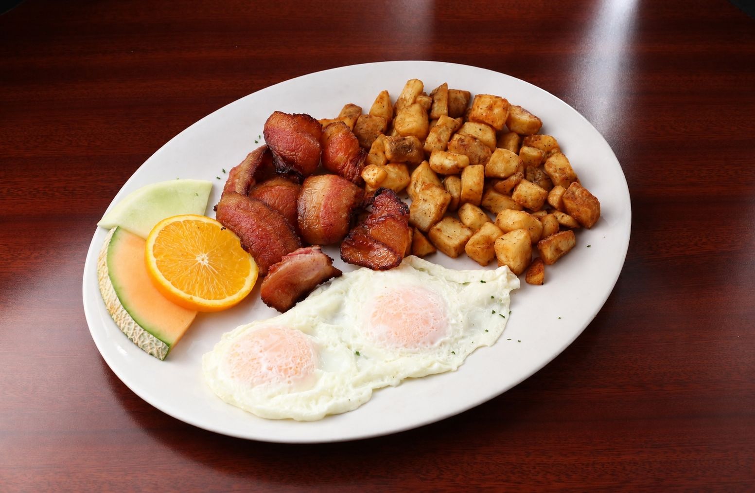 A plate of food with bacon, potatoes, eggs, and fruit.