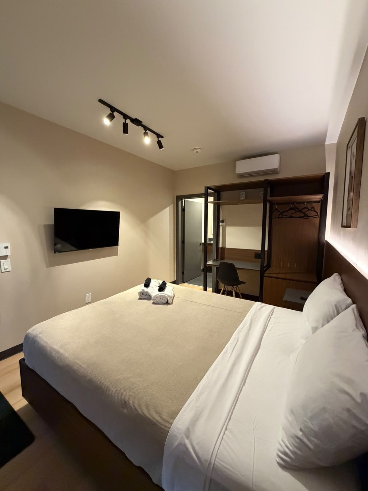 Ein Hotelzimmer mit einem großen Bett, einem flachbildfernseher an der Wand, einem Holzschrank und einem Spiegel.