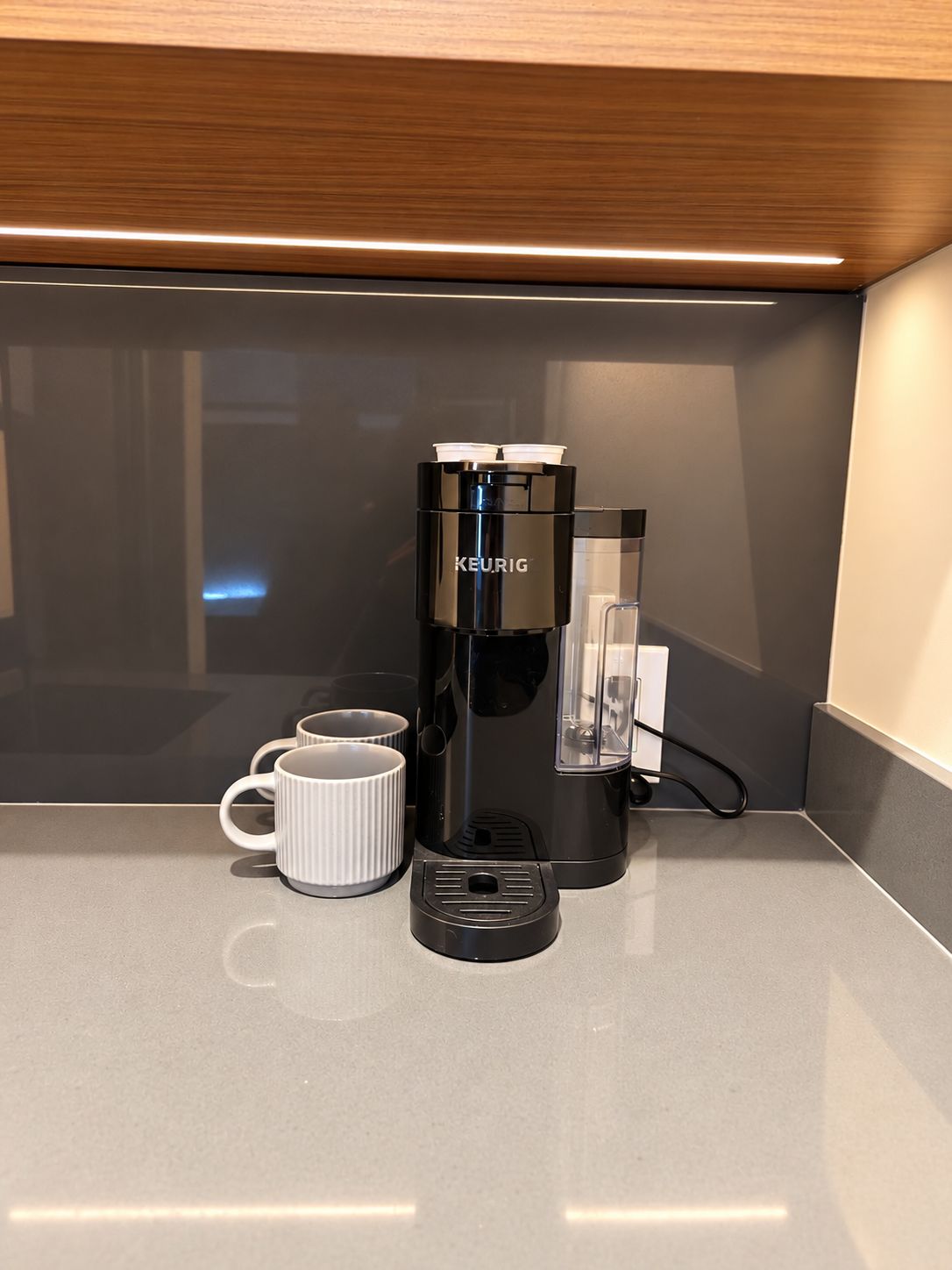 Une machine à café Keurig posée sur un plan de travail, avec deux tasses blanches à côté.