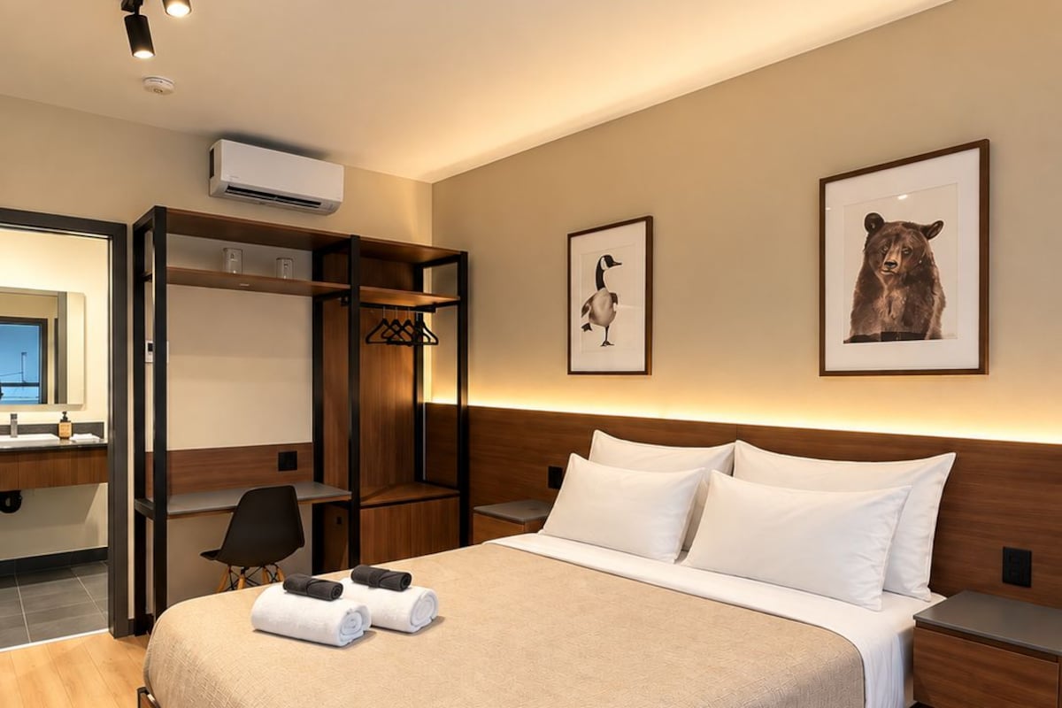A hotel room with a bed, a desk, a chair, a wardrobe, and a bathroom visible through an open door.