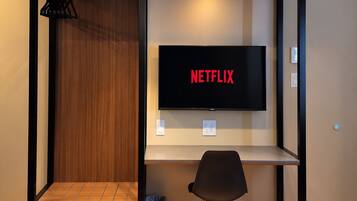 A room with a bed, a desk, a chair, a television, and a shelf.