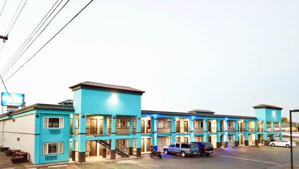 A multi-story hotel with a blue facade, multiple balconies, and a parking area with several vehicles. - Holiday Lodge Salem,OR (Salem)