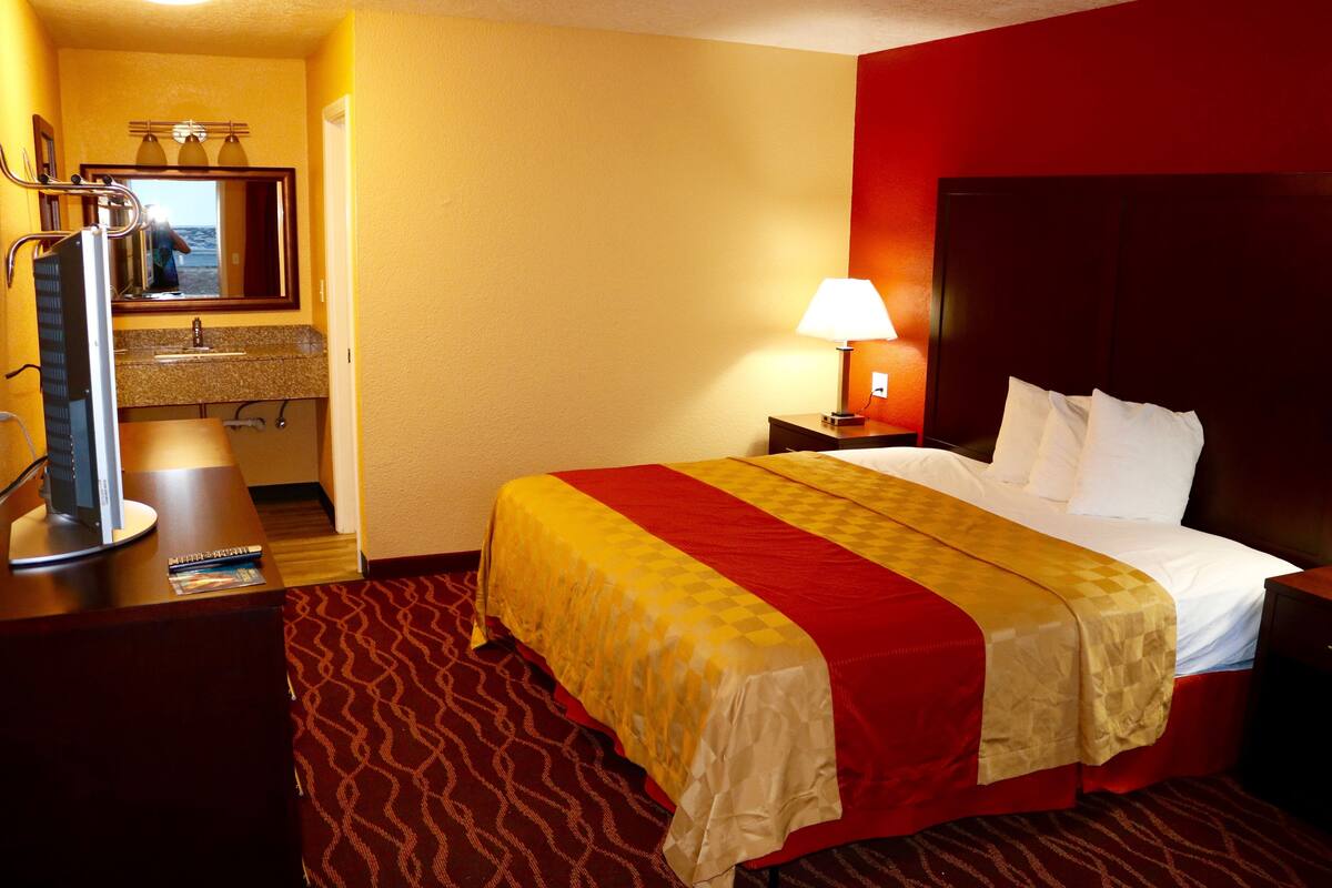 A hotel room with a bed, a desk with a computer, a mirror, and a lamp.
