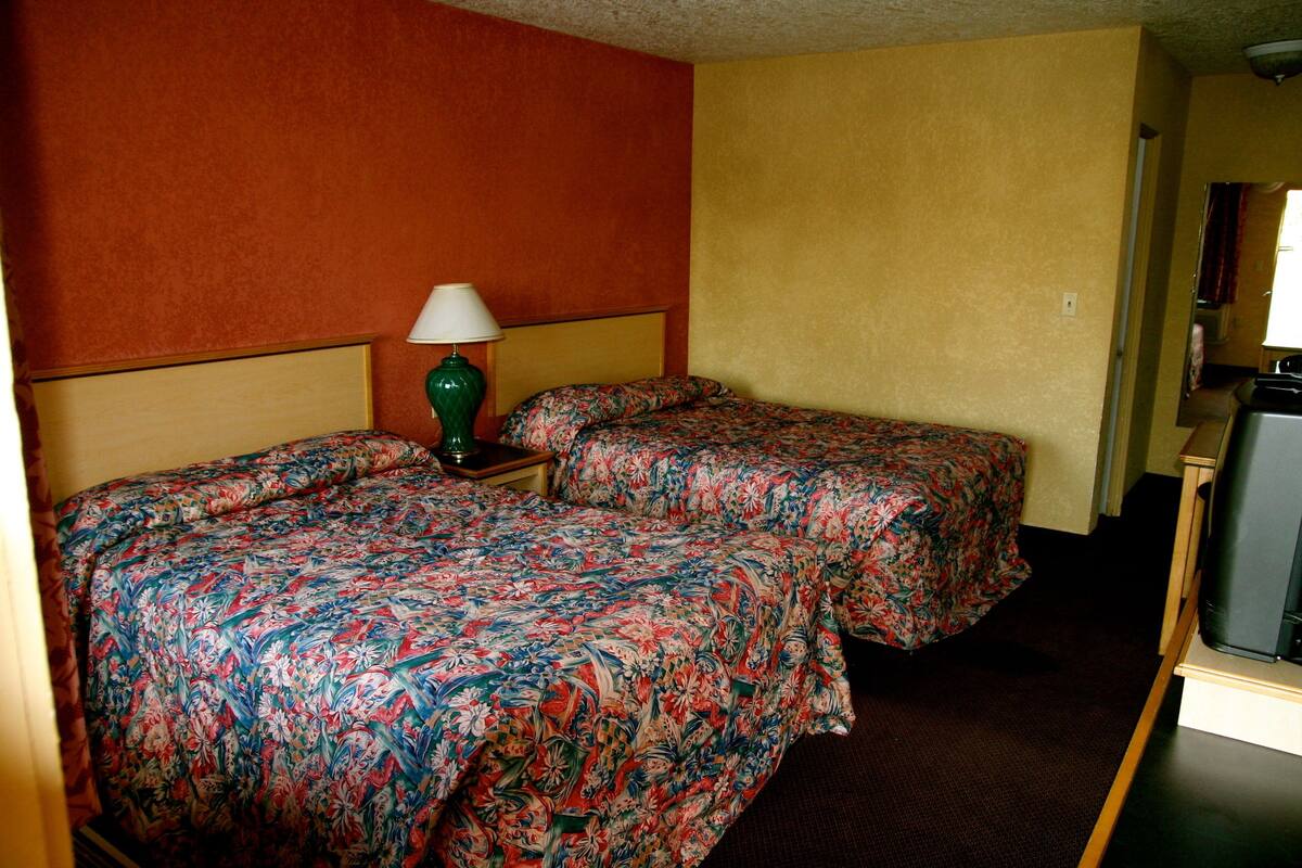 A hotel room with two beds, a nightstand with a lamp, and a television.