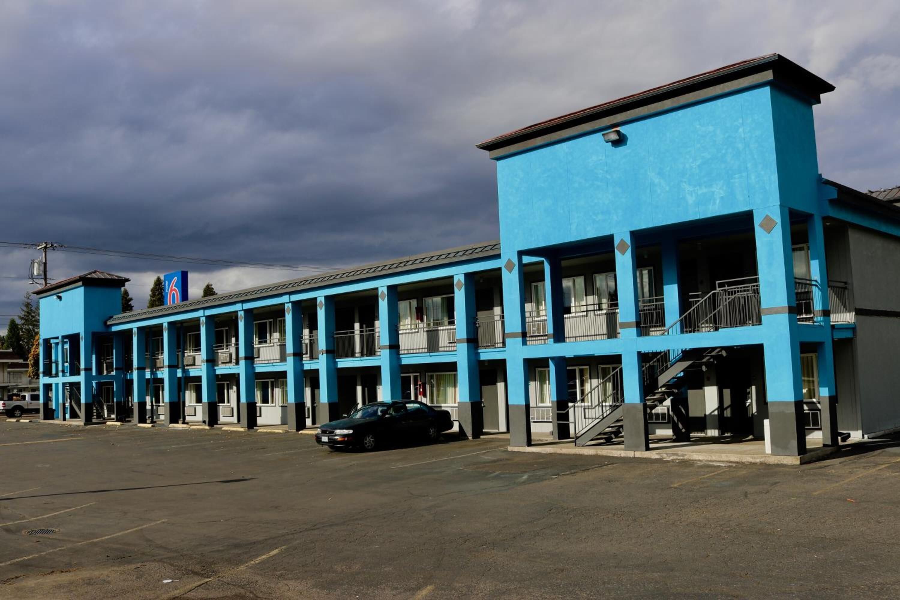 A motel with a blue exterior, multiple balconies, and a parking lot.