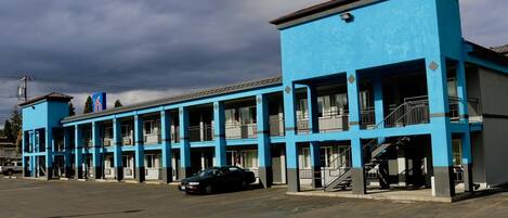 Un motel con fachada azul, varios balcones y un estacionamiento.