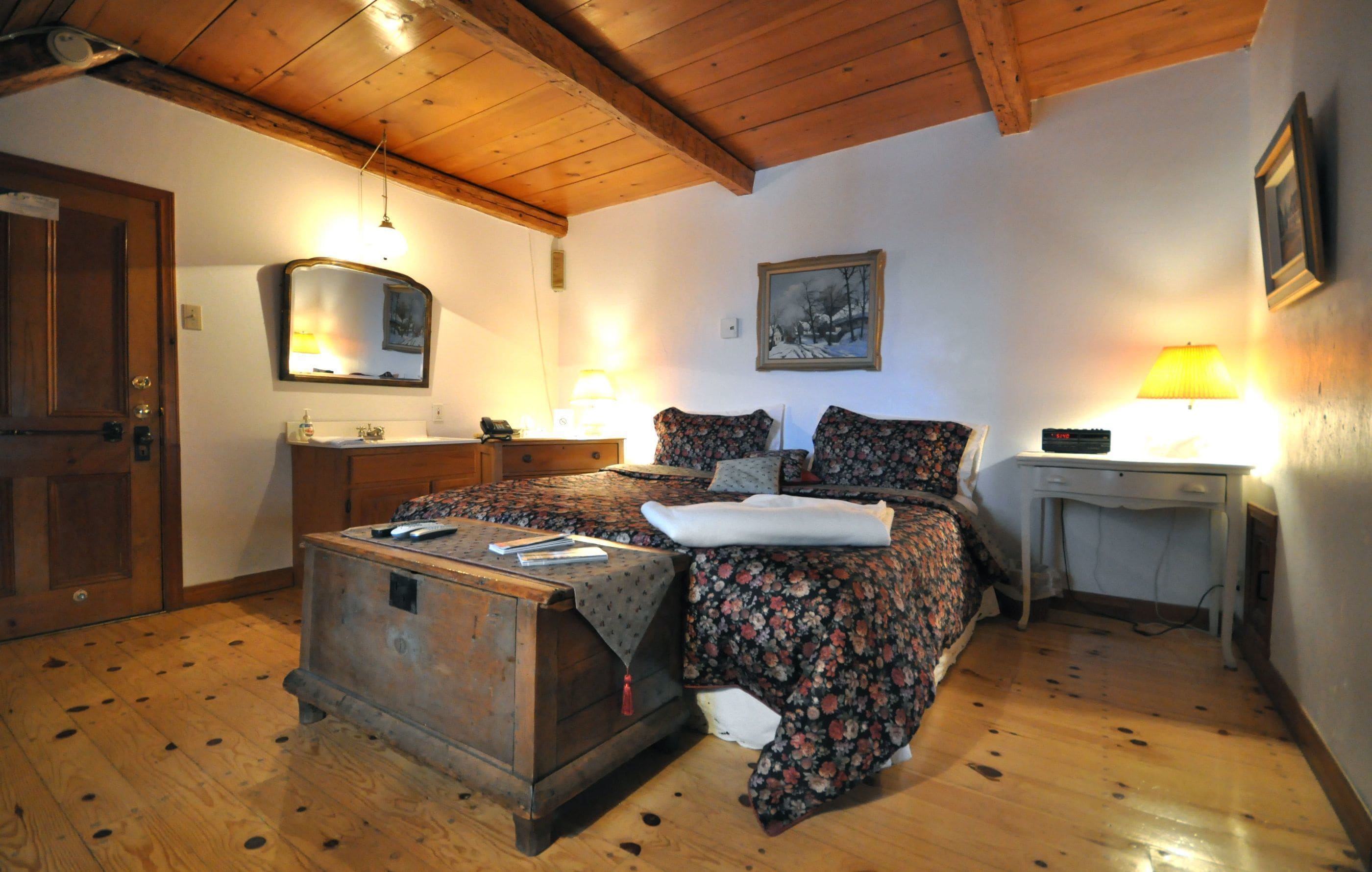A bedroom with a wooden bed, a bedside table, a desk, and a chair.