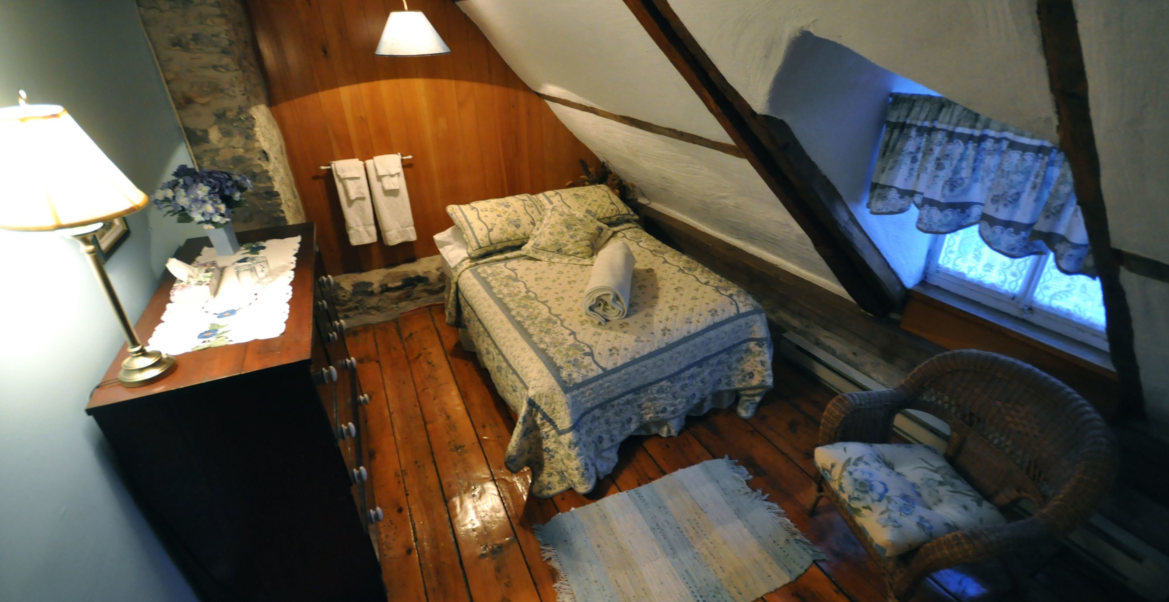 A cozy room with a bed, a chair, a desk with a lamp, and a window with curtains.