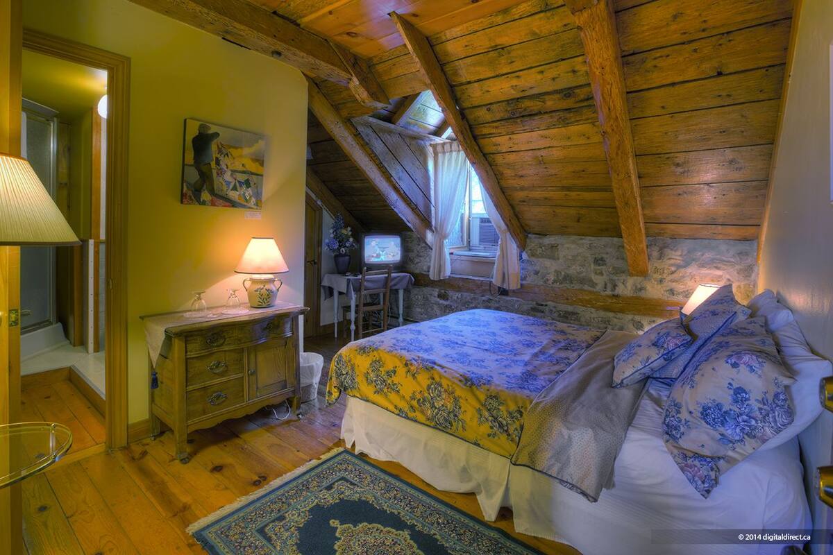 A cozy attic bedroom with a sloped ceiling, a bed with floral bedding, a desk with a lamp, and a television.