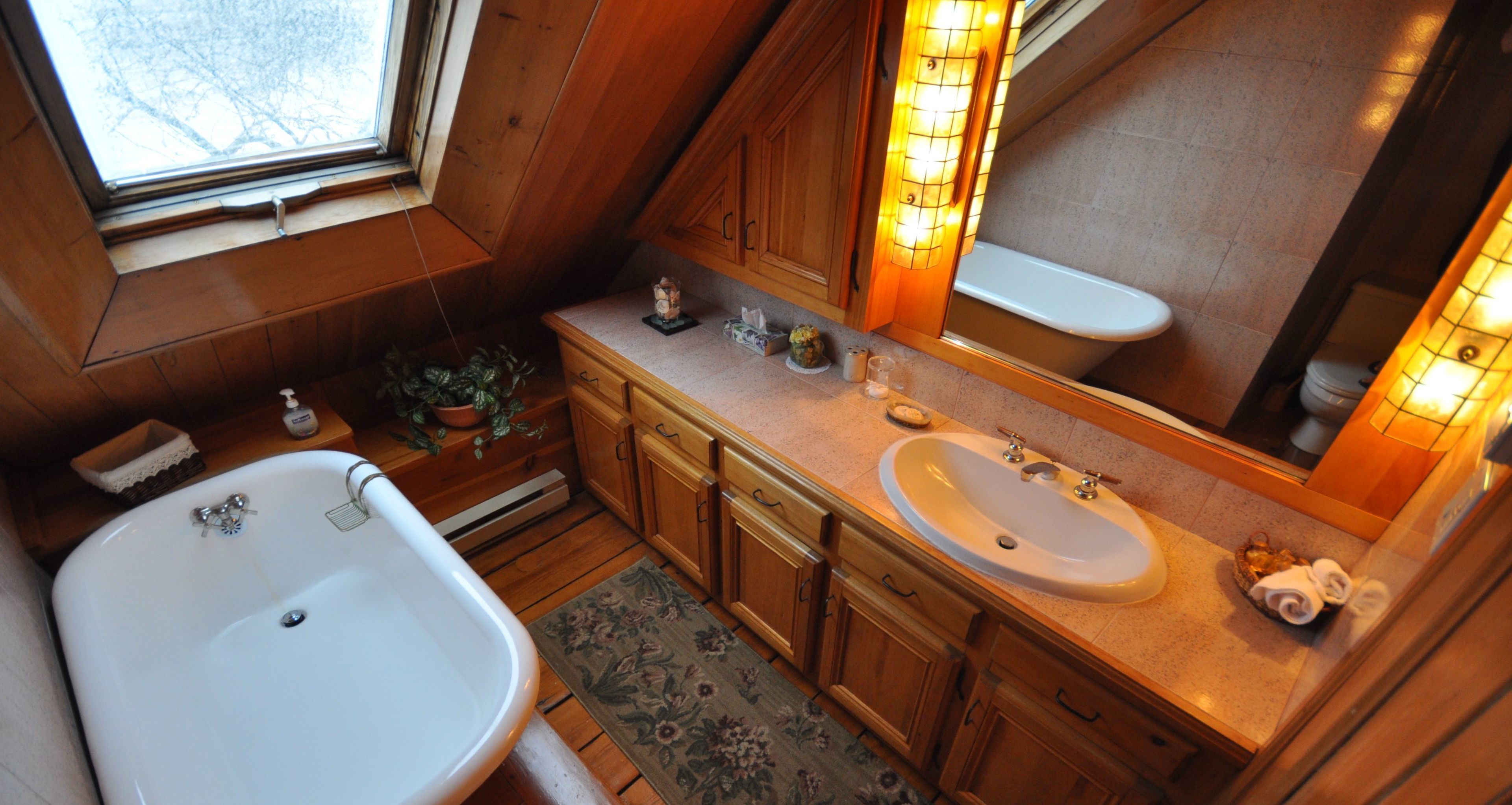 A bathroom with wooden cabinets, a white sink, a bathtub, and a large mirror with lights.