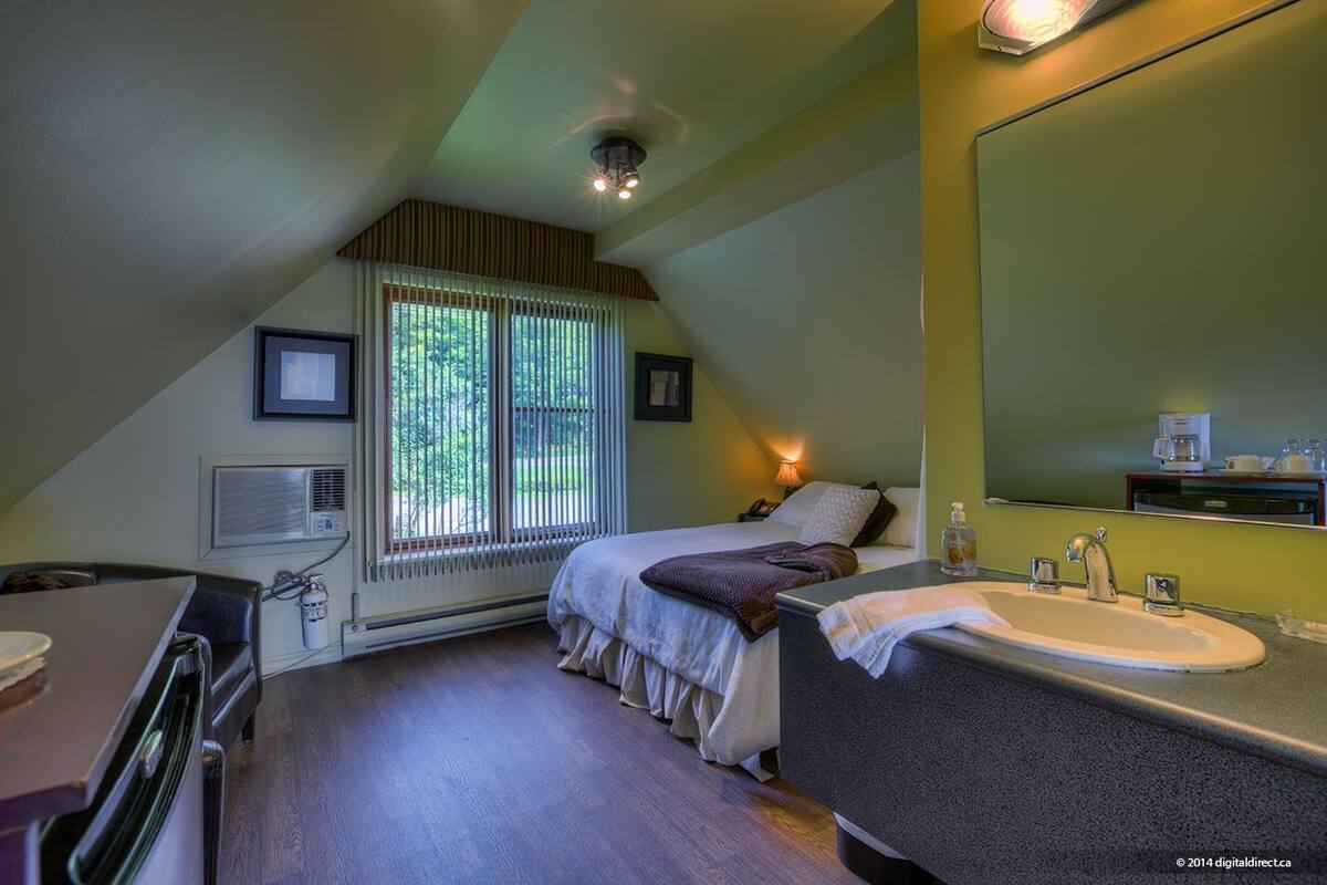 A bedroom with a bed, a bedside table, a mirror, a window with blinds, and a radiator.