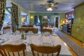 A dining area with tables set for four, wooden chairs, and a ceiling fan. - Auberge Baker (Chateau-Richer)