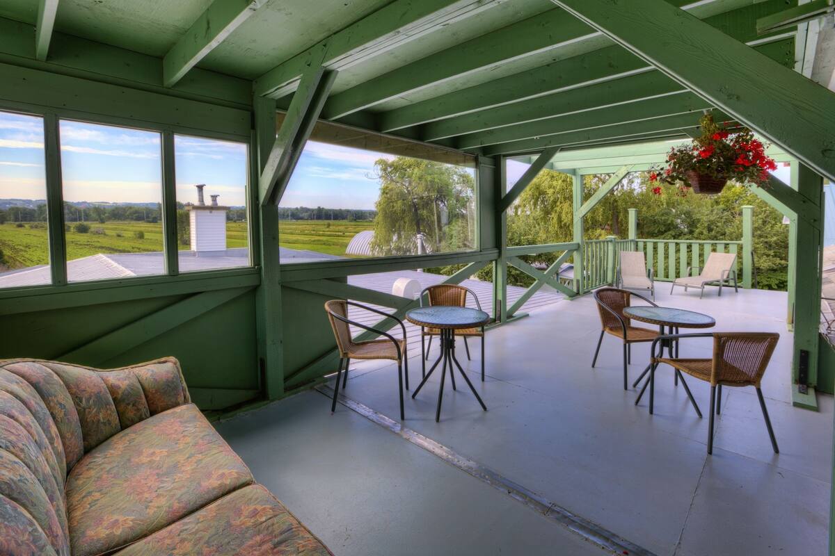 A covered patio with a green wooden structure, a cushioned bench, and a table with chairs.