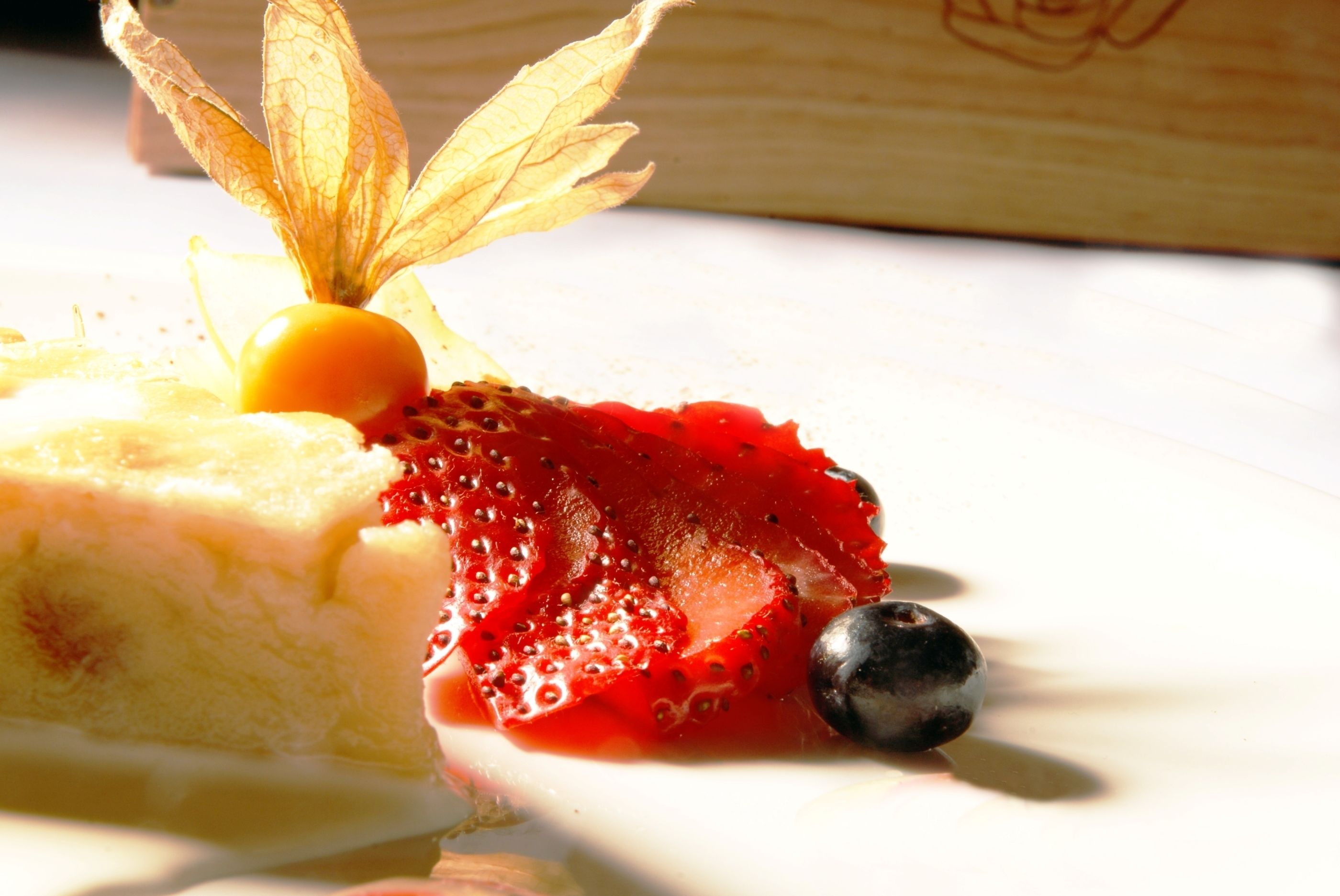 A dessert with a slice of cake, a strawberry, and a blueberry on a white plate.