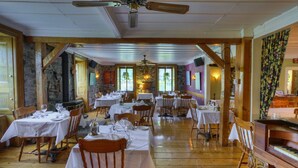 Een restaurant met houten tafels en stoelen, stenen muren en een piano.