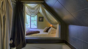 Een slaapkamer met een schuine kap, een bed met kussens, een raam met gordijnen en een wandradiator.