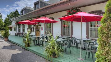 A building with a covered outdoor seating area, green flooring, and red umbrellas.