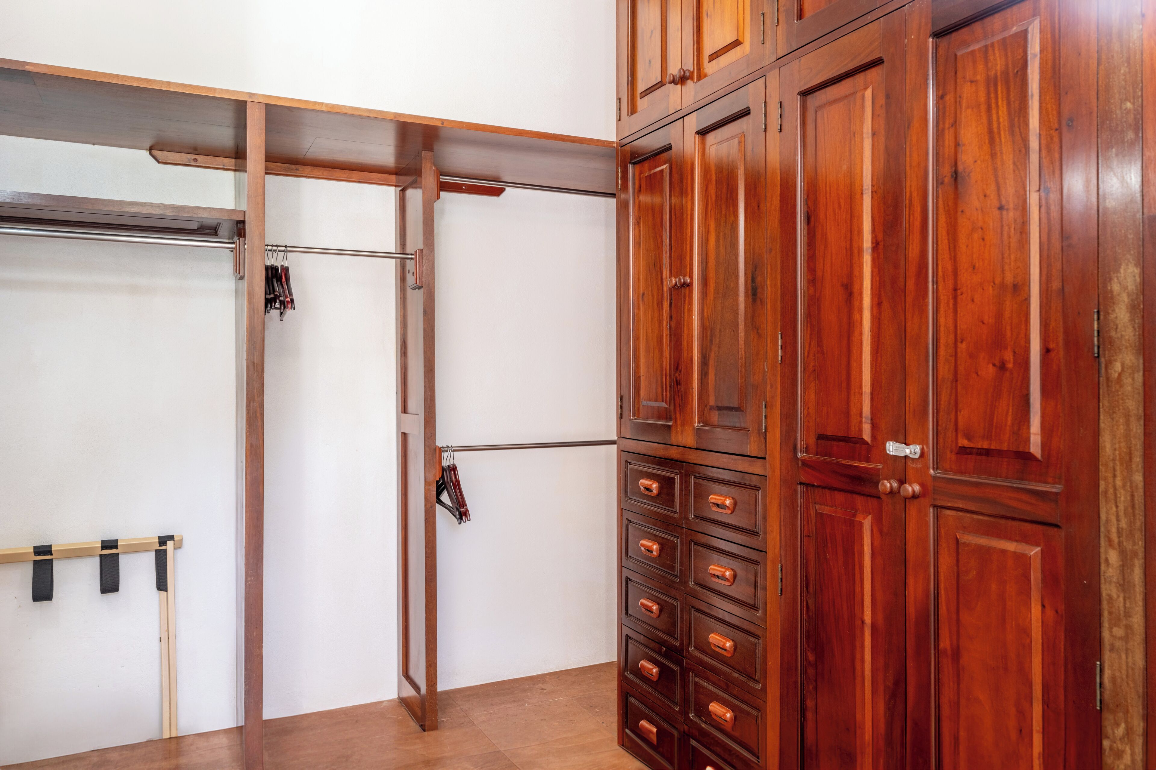 A room with a wooden wardrobe, a metal rack, and a wooden door.