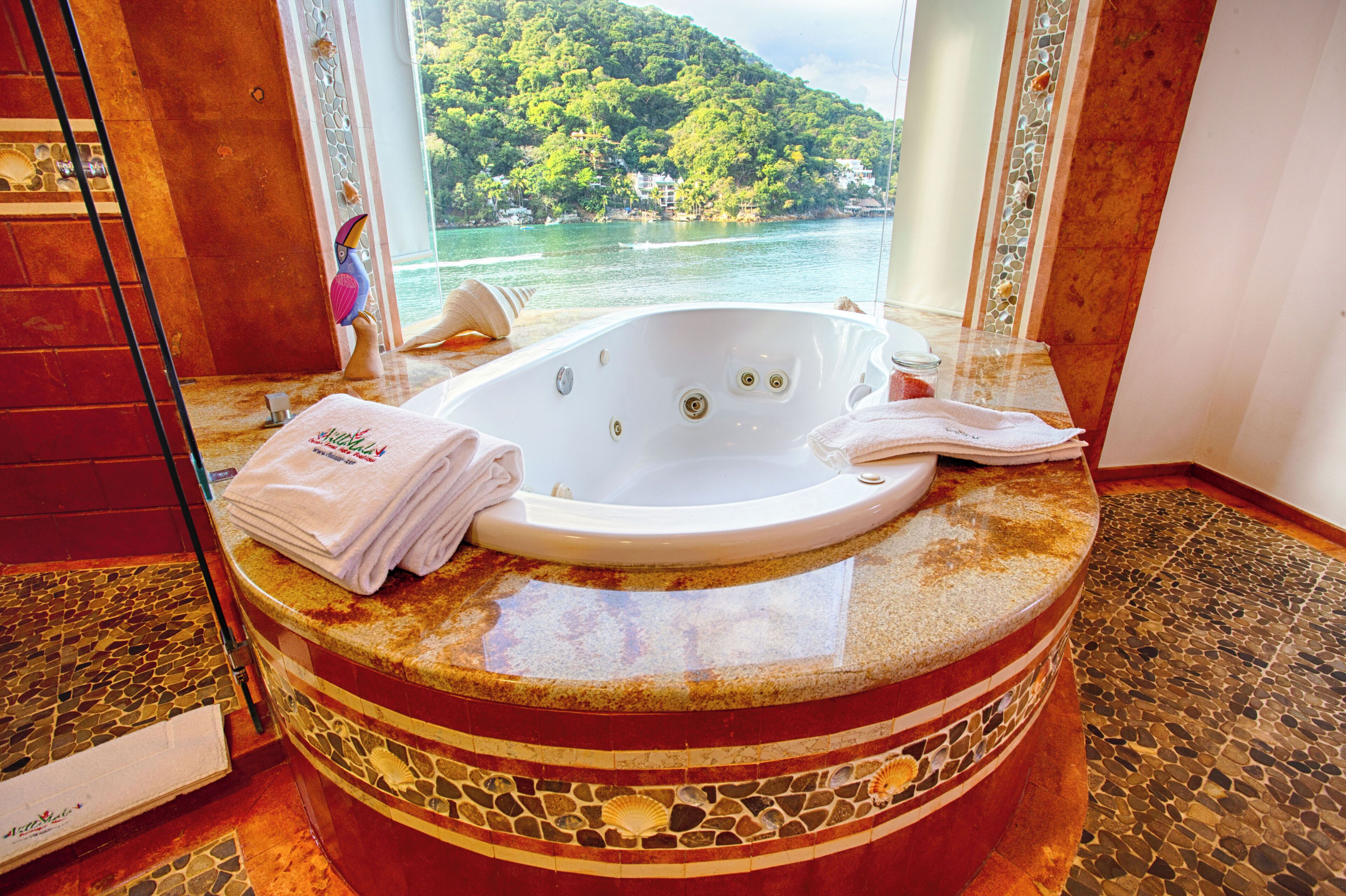 Un baño con una bañera grande, vistas a un lago y suelo de baldosas.