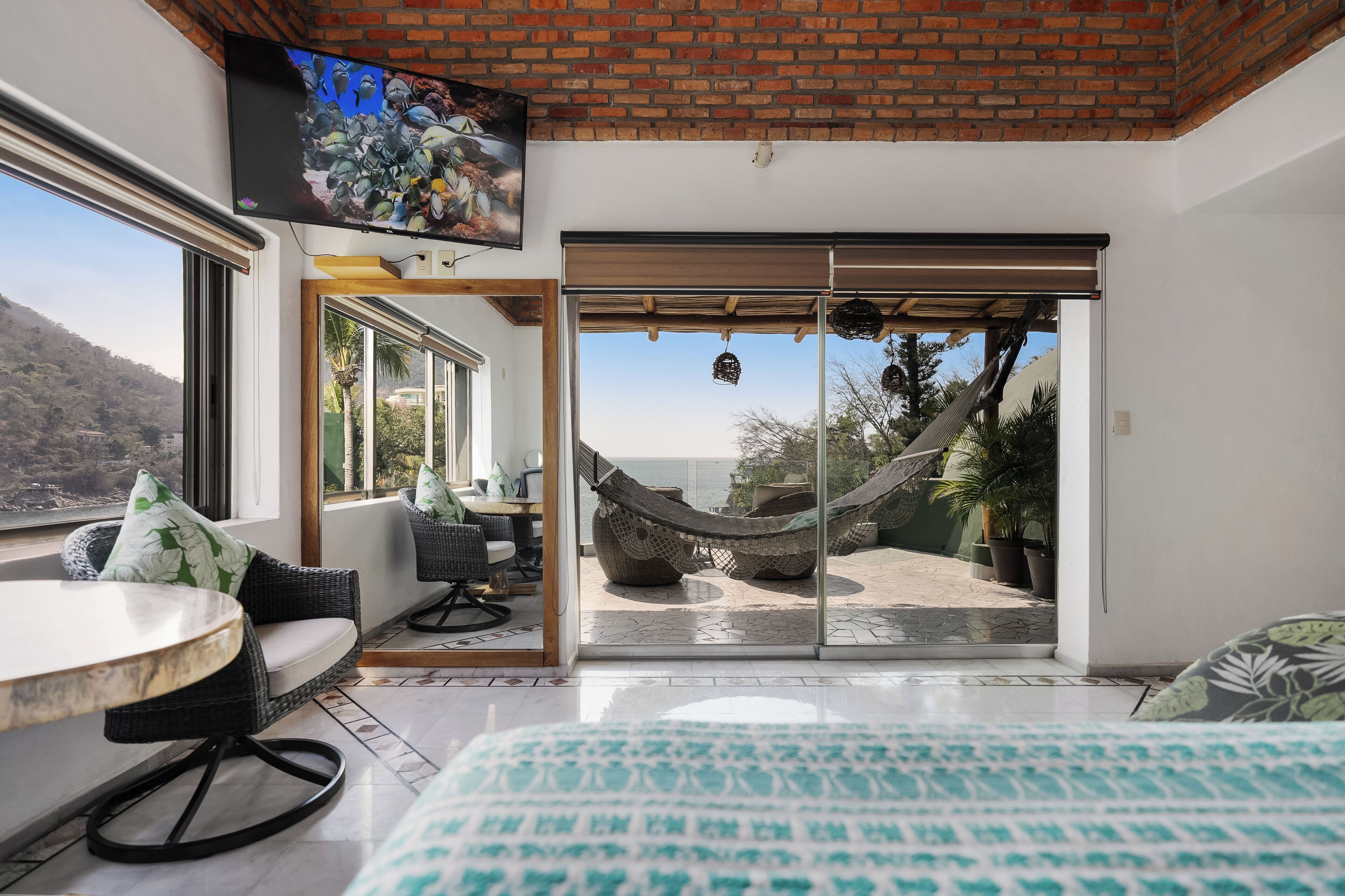 Una habitación con cama, televisión, mesa de comedor y vista a una hamaca en el exterior.