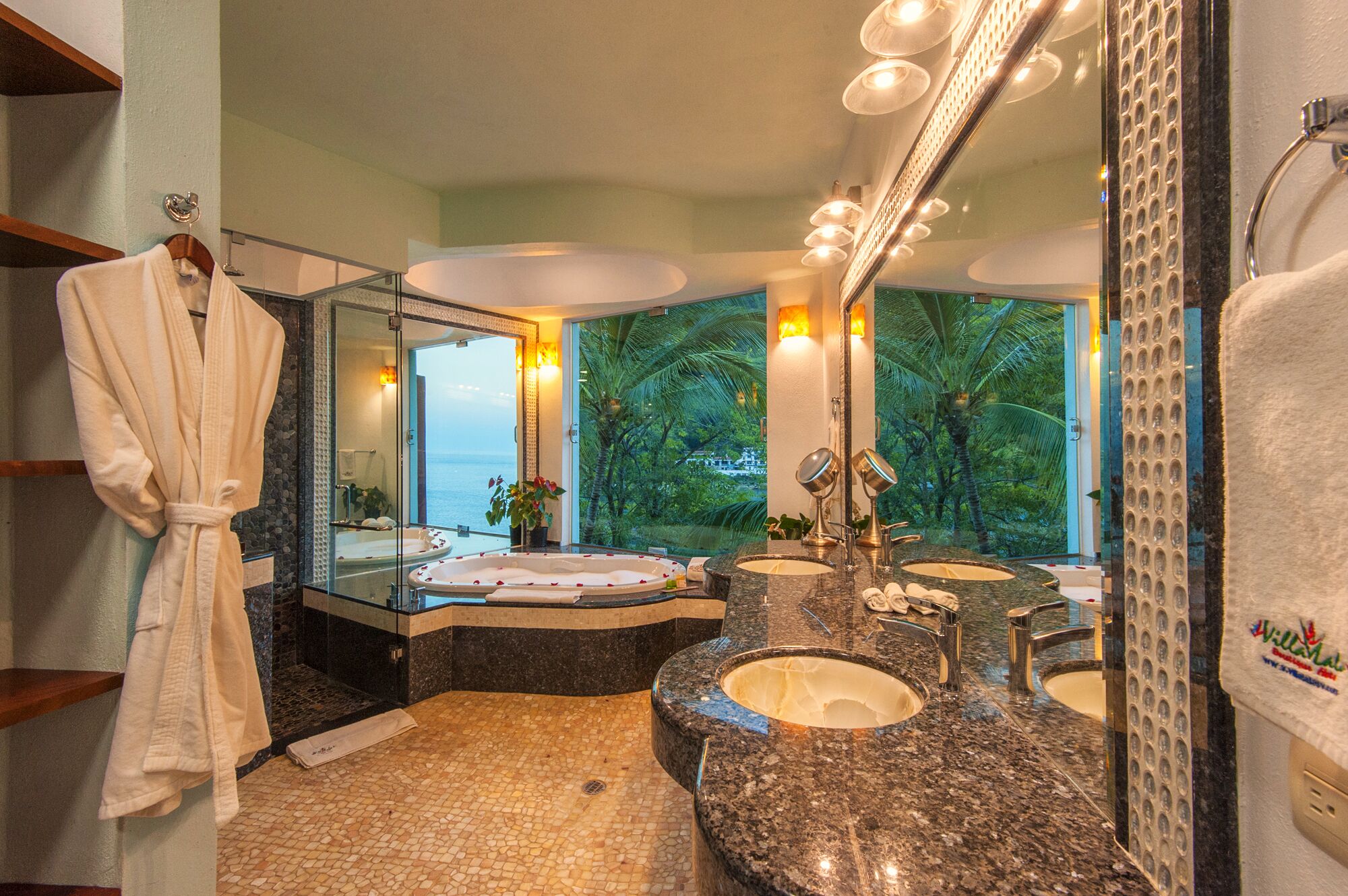 A bathroom with a large mirror, two sinks, a bathtub, and a view of the ocean.