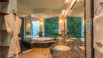 A bathroom with a large mirror, two sinks, a bathtub, and a view of the ocean.