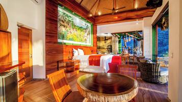 A modern room with a wooden floor, a round table, a sofa, and a bed with a red blanket.