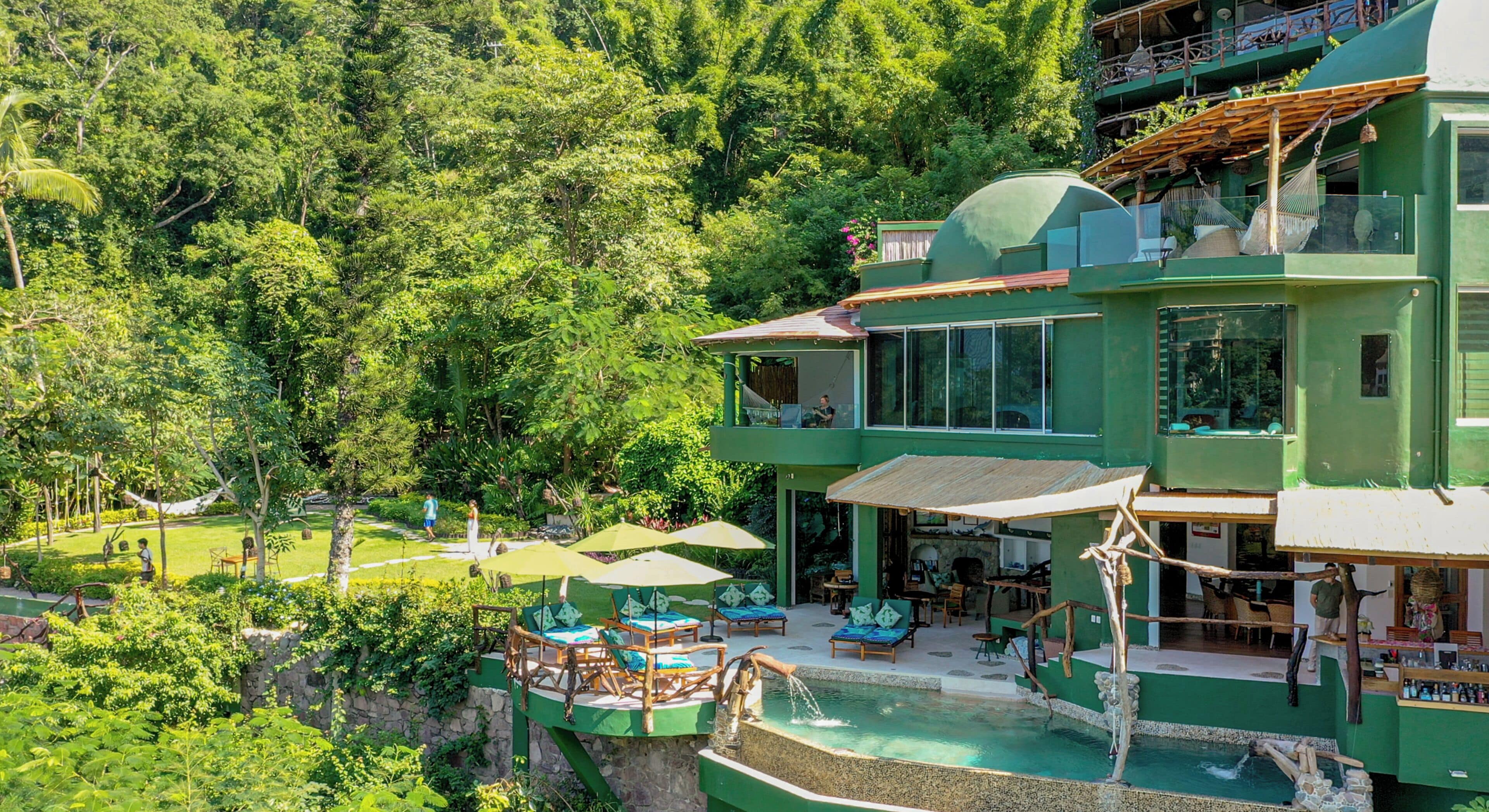 Un grand immeuble à étages, doté d’une piscine, d’un espace extérieur aménagé et entouré d’une végétation luxuriante.