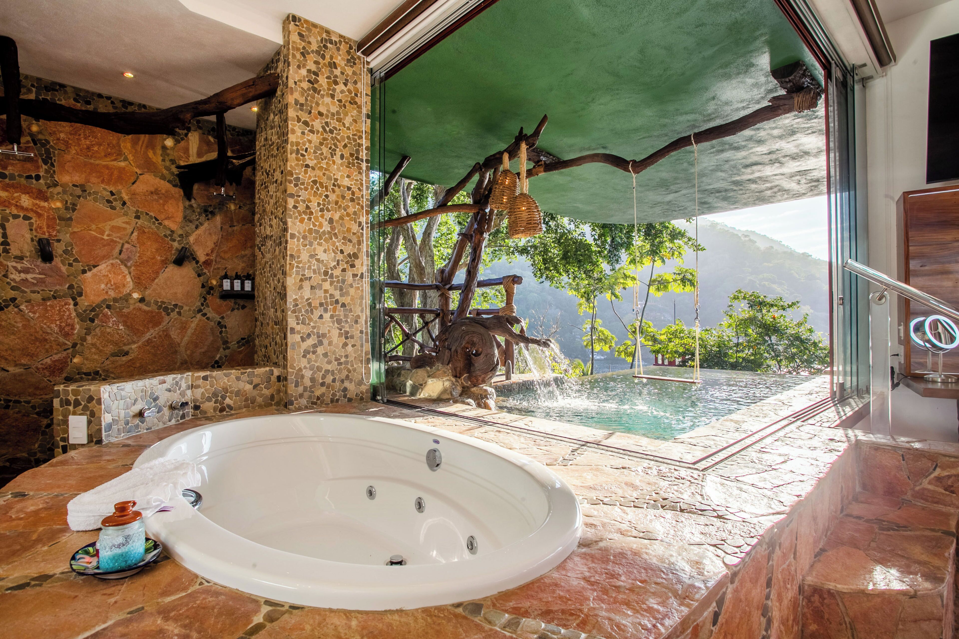Un baño con pared de piedra, una bañera y vistas a una cascada.