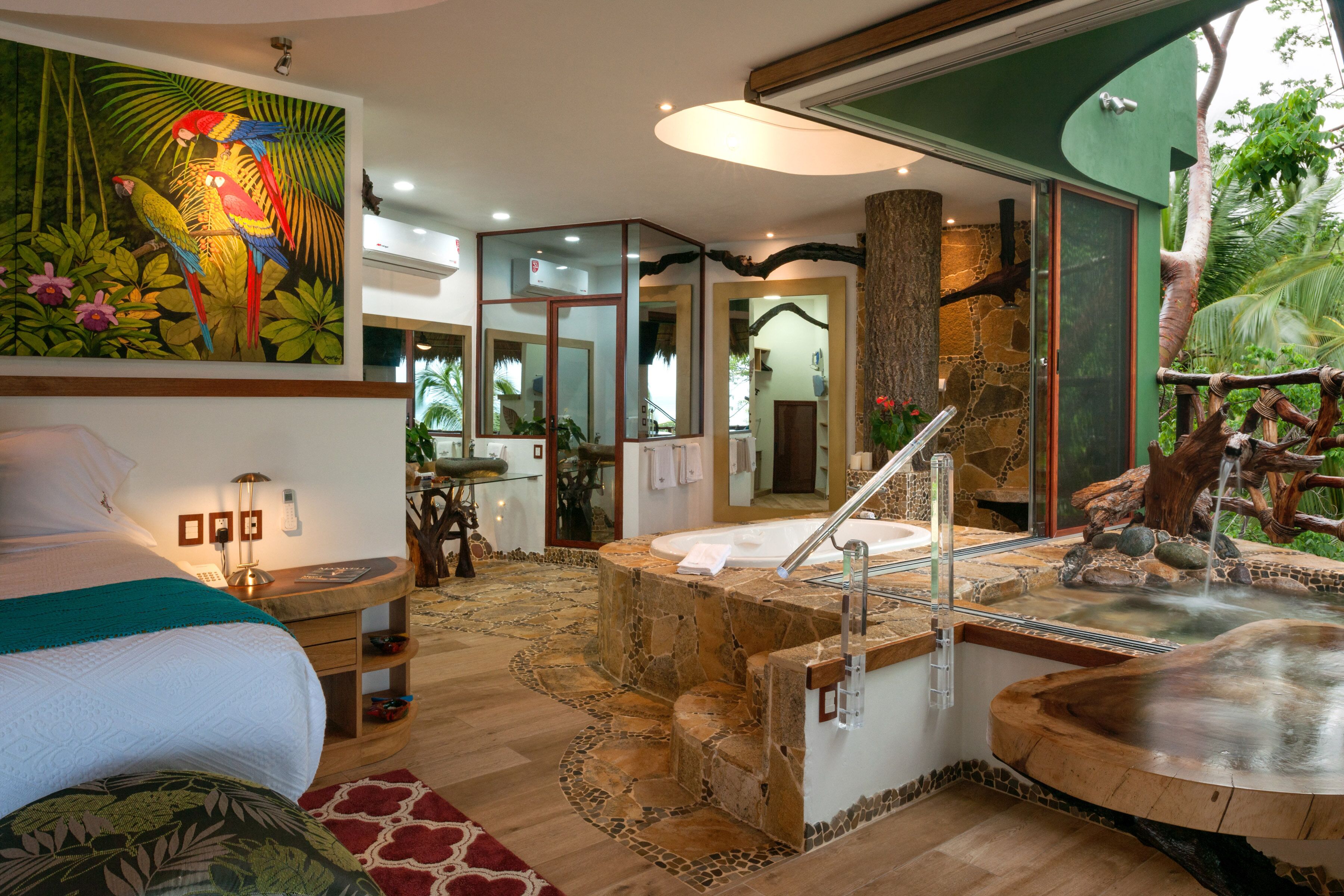 Une chambre à coucher avec un grand lit, une table de chevet en bois, un miroir et un tableau représentant des oiseaux aux couleurs vives.